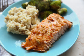 A blue plate with salmon, risotto, and broccoli. In the top left corner in the background is a fork head.