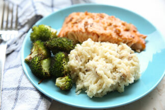 A blue plate with a serving of salmon, broccoli and mushroom Risotto. A kitchen towel is on the left side of the plate with a fork sitting on it.