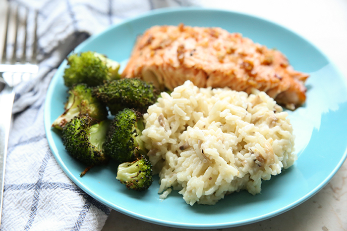 A blue plate with a serving of salmon, broccoli and mushroom Risotto. A kitchen towel is on the left side of the plate with a fork sitting on it.