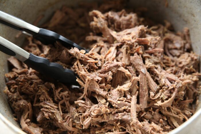 pot with shredded beef and there are tongs taking out a portion of it