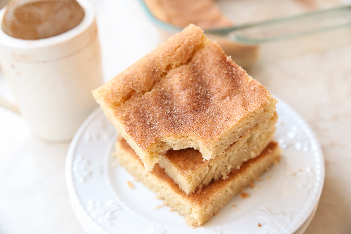 A cinnamon-sugar shaker next to a small plate with three bars stacked on top of each other with the top one having a bite out of one corner.