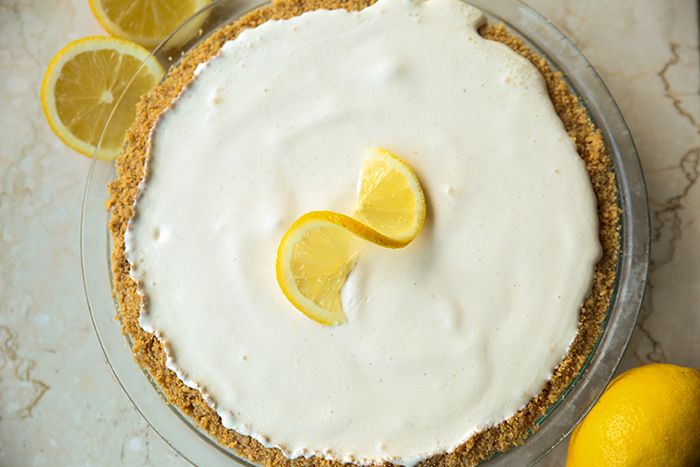 3-Ingredient Lemonade Ice Cream Pie with a twisted lemon slice on top. In two opposite corners are a whole lemon and a lemon cut in half.