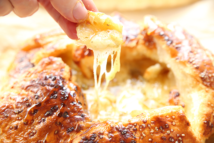 A hand holding a piece of puffed pastry held above Gruyere puffed pastry bake.