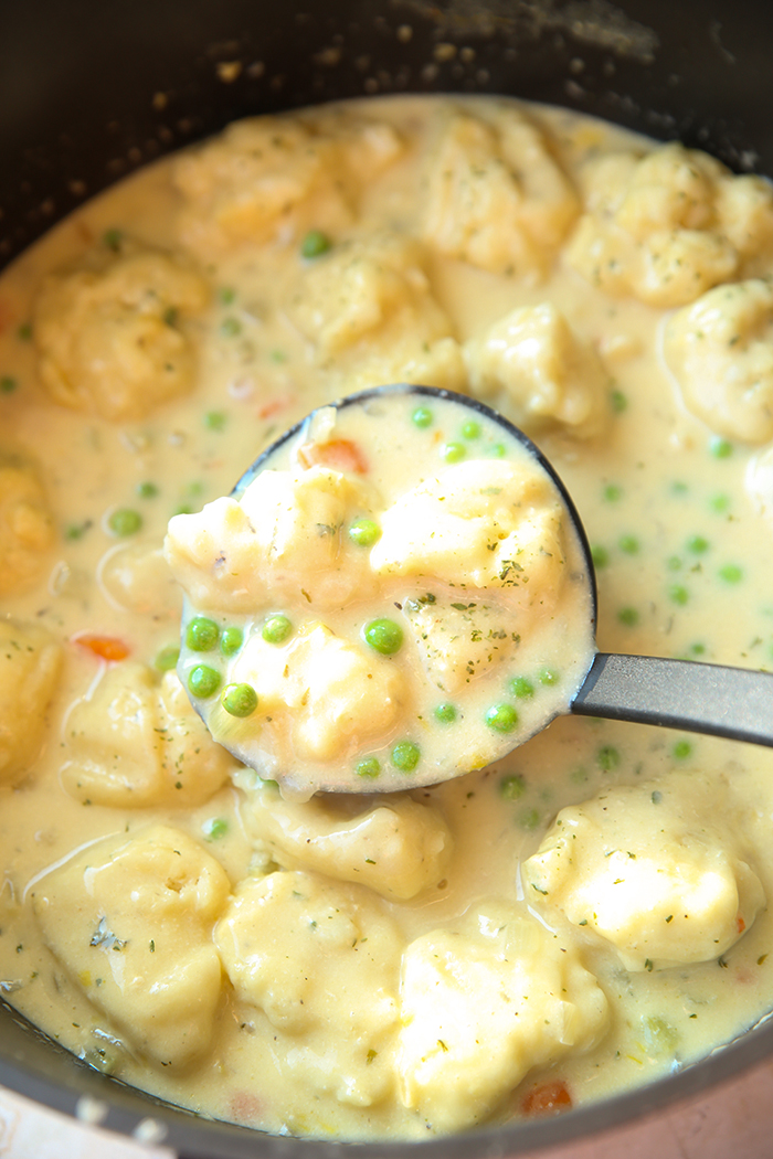 A large soup pot of Creamy Chicken and Dumplings Soup with a ladle of soup held above it.