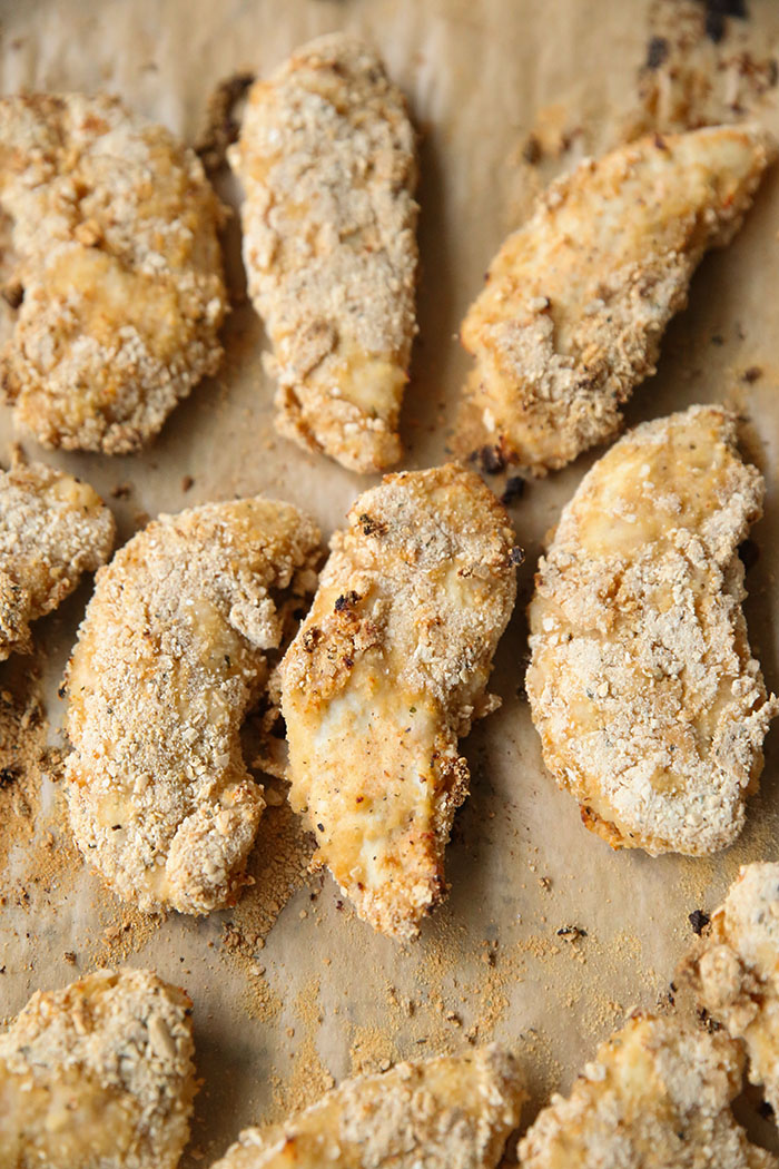 Easy Baked Chicken Fingers sitting on brown parchment paper on a baking sheet.