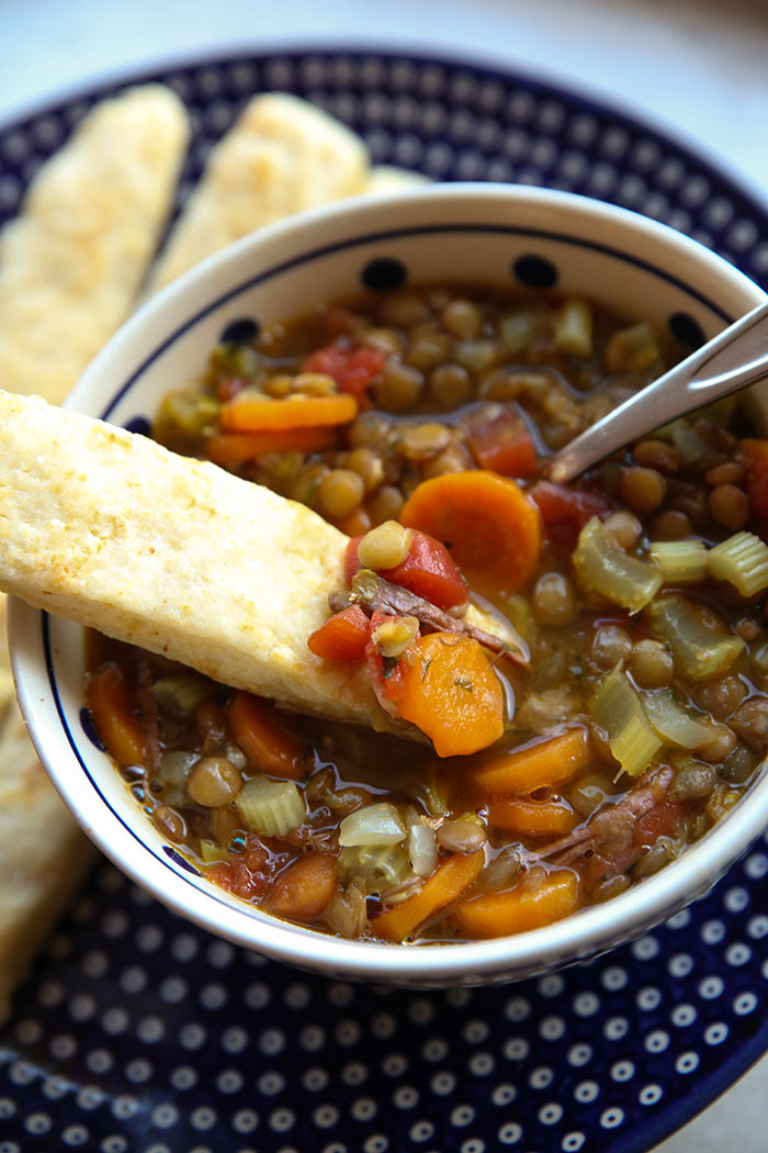 bowl of lentil soup with a delicious baking powder breadstick being dipped in it. You can see a few more breadsticks in the background