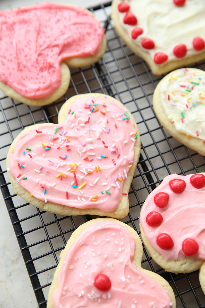 Six sugar cookies heart-shaped, frosted and decorated with Red Hots and sprinkles.