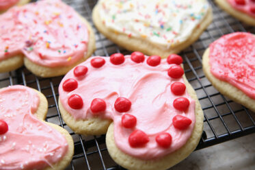 Heart-shaped sugar cookies frosted and decorated sitting on a black wire cooling rack.