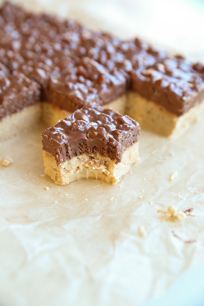 Peanut butter crunch bars cut into squares with a few pieces missing to make a stair-like appearance. One crunch bar is placed in front with a bite taken out of the corner.