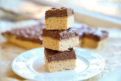 A stack of three chocolate peanut butter crunch bars sitting on a white plate with the remaining cut bars in the faded background.