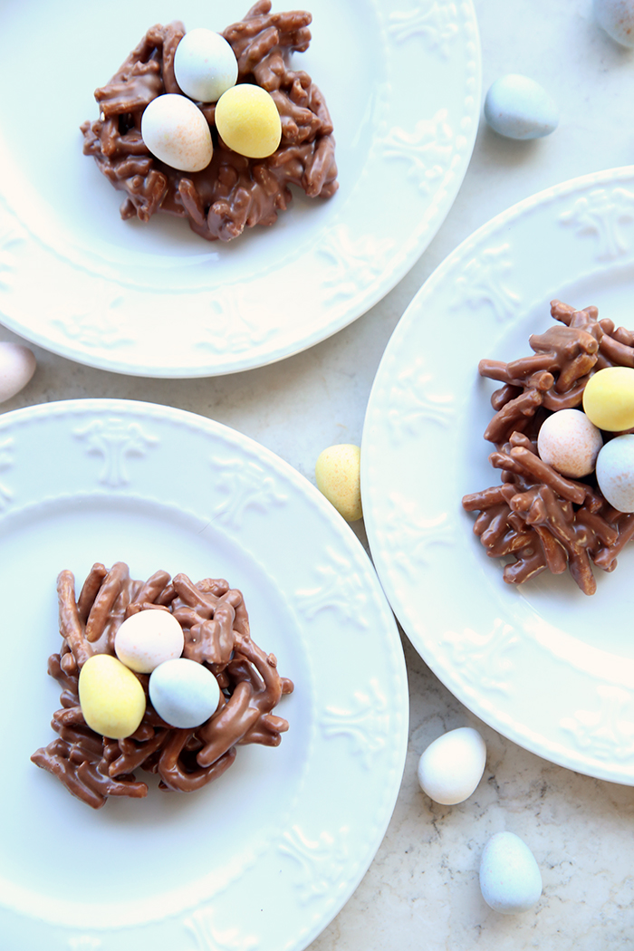 No-bake Birds Nest Cookies with a cookie on three small white plates. Cadbury Mini Eggs are scattered around the plates.
