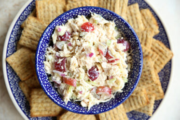 A Polish pottery bowl full of Classic Chicken Salad with Grapes on a large plate surrounded by triscuit crackers.