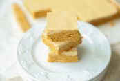 Three cut peanut butter bars stacked offset on top of each other on top of several plates. Faded in the background are more cut double peanut butter bars on parchment paper.