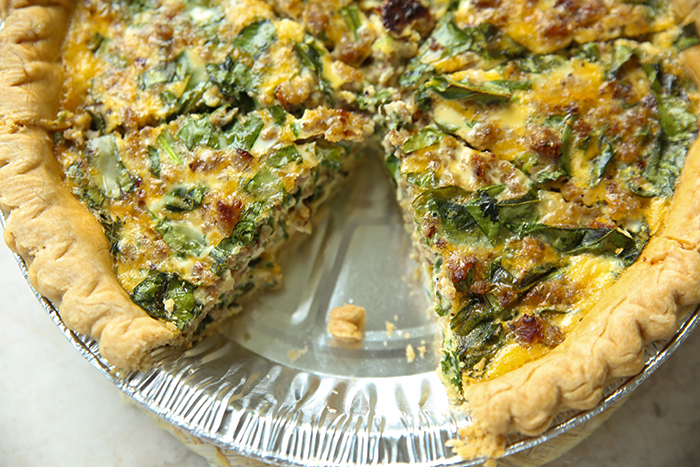 A sliced Spinach and Sausage Quiche with a piece missing from the pan.