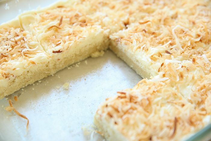A glass 9x13 dish of coconut swig sugar cookie bars cut into squares with three pieces missing from the dish.