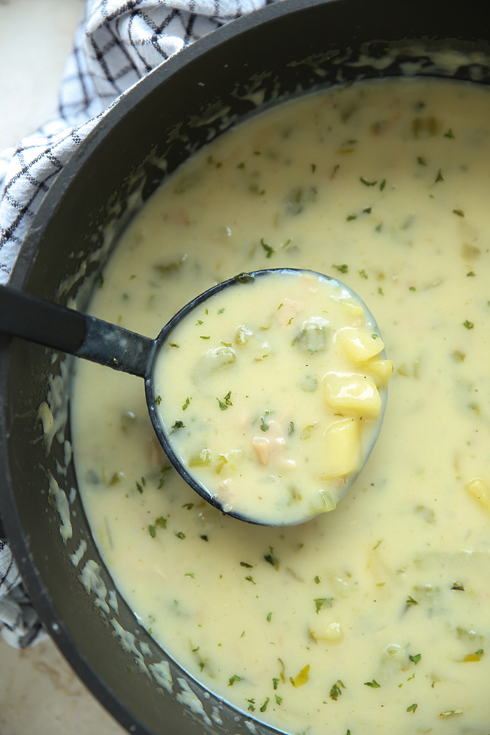 A large pot of Classic Clam Chowder with a soup ladle with chowder held above the chowder.