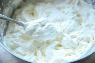 A large metal bowl full of homemade whipped cream with a spoon of whipped cream held above from the left.