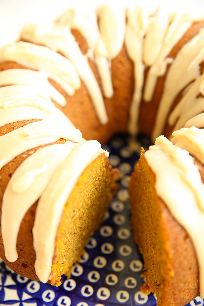 A pumpkin bundt cake with brown butter icing dripped down the sides on a large blue and white patterned Polish pottery plate with a slice cut out.