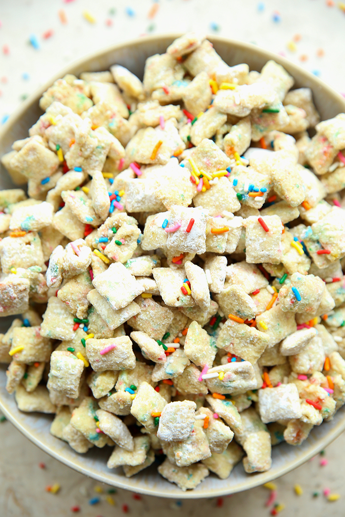 Funfetti cake mix Chex mix in a large bowl with rainbow sprinkles scattered around the whole bowl.