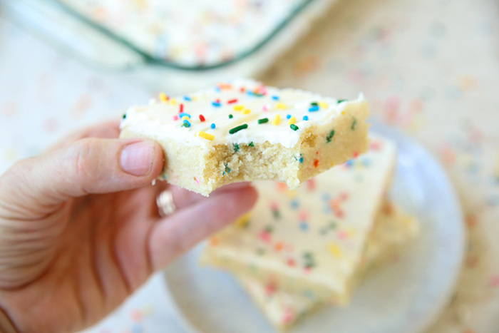 sprinkle loaded funfetti cookie bars topped with swig buttercream and more rainbow sprinkles