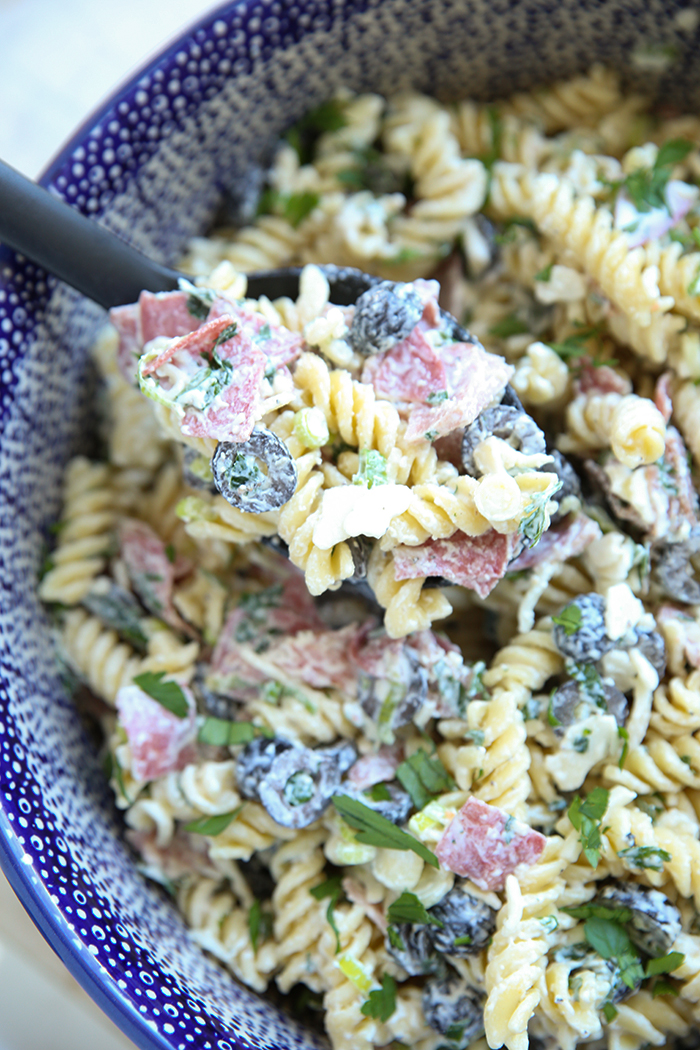 large blue bowl filled with pasta salad that has salami and olives