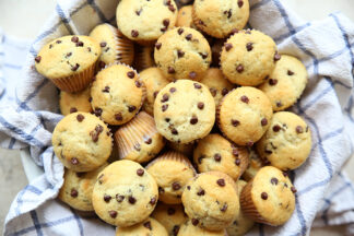 A kitchen towel lined bowl filled with chocolate chip mini muffins.