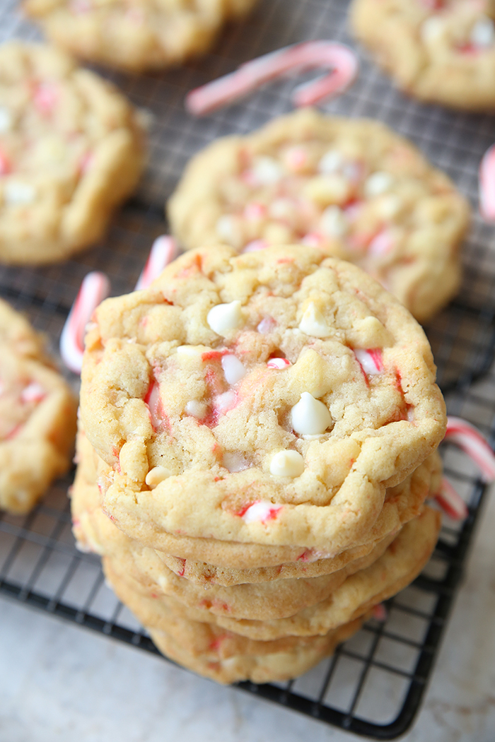 A wire cooling rack of white chocolate peppermint cookies and a few small candy canes with several cookies stacked in one corner.