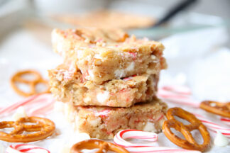 A stack of three white chocolate peppermint pretzel cookie bars surrounded by twist pretzels and small candy canes.