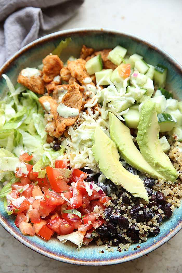 Chicken Quinoa Burrito Bowl with pico de Gallo, black beans, chopped lettuce, cucumber and sliced avocado, topped with shredded cheese and dressing.