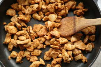 Bite-size chicken taco meat in a nonstick skillet with a wooden spatula inserted on the right.