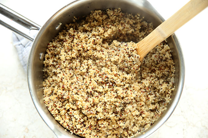 A pot of quinoa with a wooden cooking spoon inserted at an angle on the right.