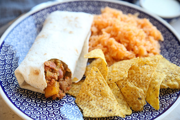 A dark blue patterned Polish pottery plate with tortilla chips, Spanish rice, and Mar's burrito with a bite taken out of it.