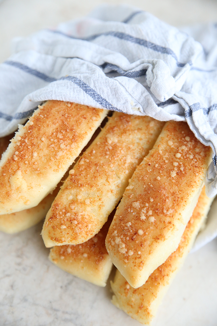 Six garlic parmesan breadsticks wrapped partially in a white and blue striped kitchen towel.