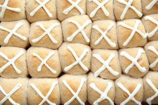 A close-up of a large baking sheet of hot cross buns frosted with an "X"