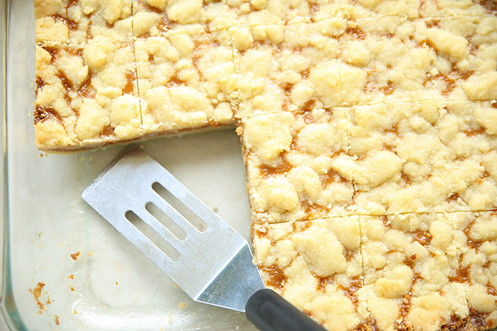 A glass 9x13 baking dish of cut caramel crush bars with a few squares missing from the left corner with a small serving spatula sitting in the empty corner.