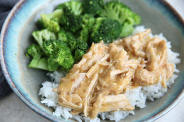 A soup bowl with steamed broccoli and shredded pork and gravy served over long-grain rice.