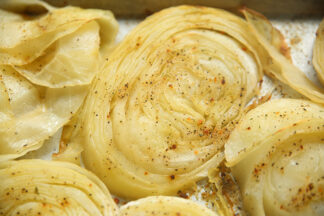 A sheet pan placed horizontally with roasted sliced cabbage pieces with seasoning.