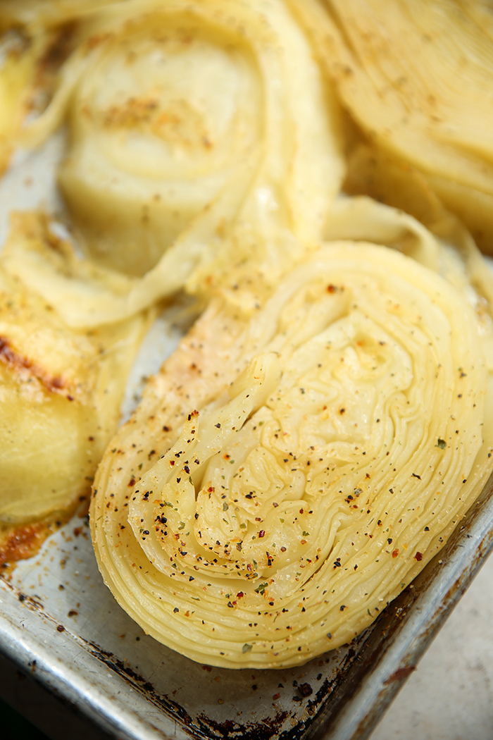 A large sheet pan with roasted cabbage steaks with seasoning on top.