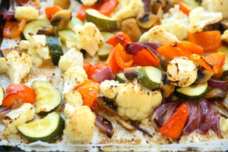 A parchment paper lined cookie sheet with roasted cauliflower, Zucchini, red bell pepper, purple onion, and mushrooms.