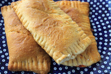 Three crescent dough pizza pockets sitting on a dark blue plate with white polka dots.