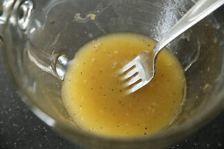 A glass bowl of balsamic honey mustard dressing with a fork inserted from the right.