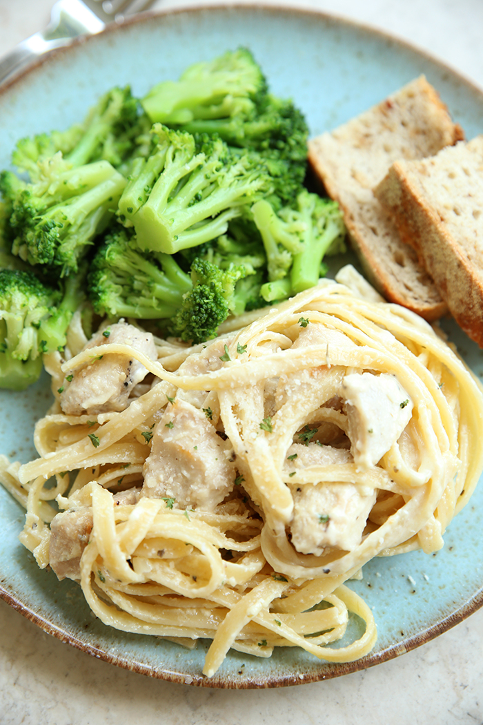A serving of lemon chicken fettuccini, broccoli, and two slices of ciabatta bread on a light blue plate.