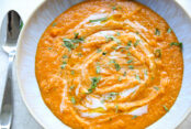 A bowl of red lentil curry soup with a spoon on the left side of the bowl.