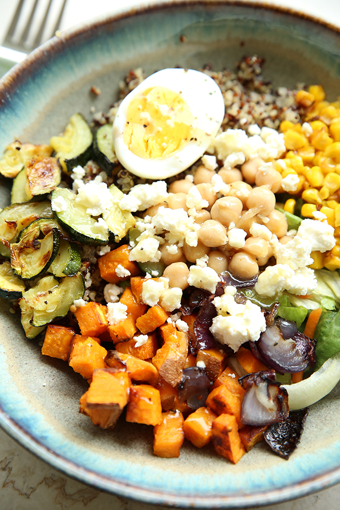 A sweet potato quinoa bowl topped with garbanzo beans, feta cheese, and a half hard-boiled egg. A fork head is in the upper left corner.