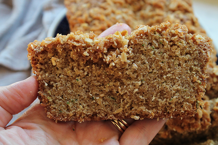 A slice of zucchini bread with streusel held above a loaf of zucchini bread.