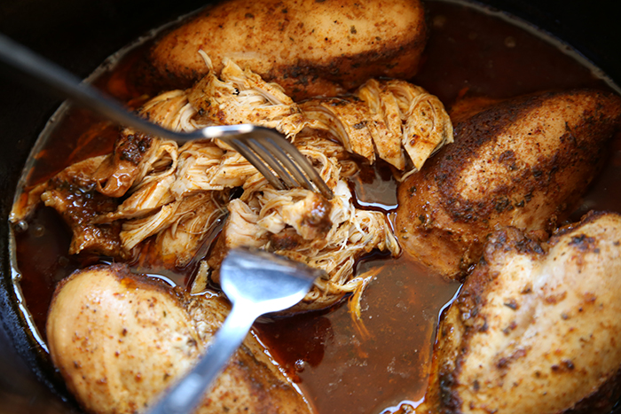A crockpot of cafe rio chicken breasts with two forks inserted into a partially shredded chicken breast.