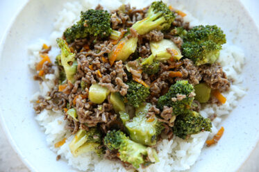 A dinner plate of ground beef broccoli with shredded carrots served over white rice.