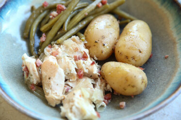 A dinner bowl plate with three baby potatoes, chopped chicken and green beans with bacon bits.