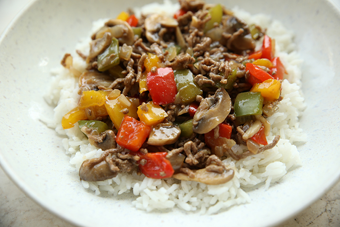 A serving of ground beef and peppers over rice on a dinner plate.