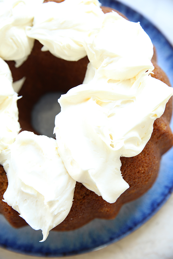 A pumpkin bundt cake topped with dollops of cream cheese closely together sitting on a large round plate.
